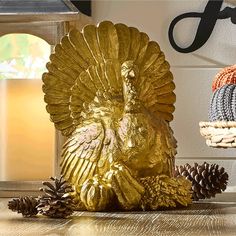 a golden turkey sitting on top of a wooden table next to pine cones and a lamp