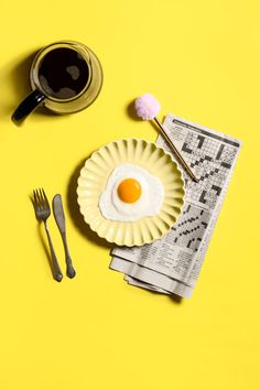 an egg on a plate next to a cup of coffee and utensils with spoons