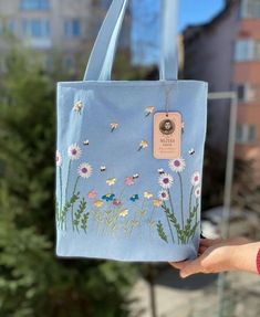 a hand holding a blue bag with flowers painted on it