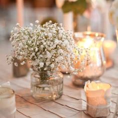 small vases filled with baby's breath flowers sit on a table next to candles