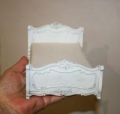 a person holding up a miniature white bed