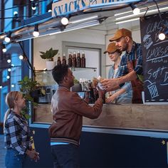 two men standing at a food stand with bottles on the counter and one man handing something to another man