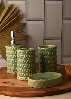 three green bathroom accessories sitting on top of a wooden table next to an orange bowl