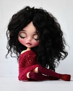 a doll with long black hair is sitting on the floor and has her eyes closed