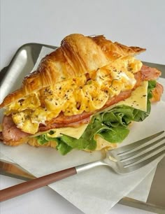 a sandwich with ham, cheese and lettuce is on a plate next to a fork