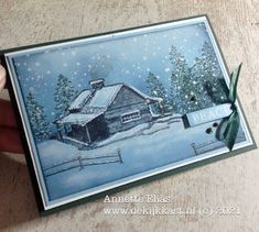 someone holding up a christmas card with a barn in the snow and evergreens on it