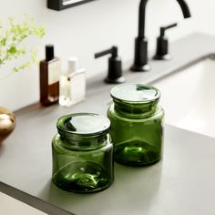 two green glass jars sitting on top of a counter next to a faucet