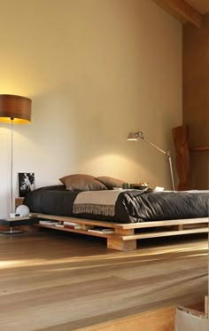 a bed sitting on top of a wooden floor next to a lamp