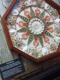 a wooden table topped with a clock covered in shells and flowers next to a plaque