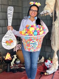 a woman is holding a bucket full of candies and plastic spoons with decorations around her