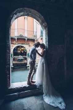 a bride and groom kissing in front of an arched window at their venice wedding venue