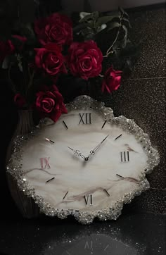 a vase with roses in it sitting on a table next to a clock and flowers