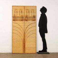 a tall wooden door sitting next to a black statue in front of a white wall