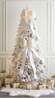 a white christmas tree decorated with gold and silver ornaments, bows and presents around it