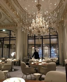 a chandelier hanging from the ceiling in a restaurant with tables and chairs around it