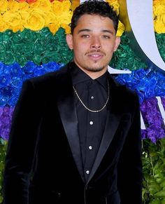 a man in a tuxedo standing next to a colorful wall with flowers on it