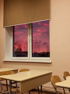 an empty classroom with desks and chairs in front of a window that has a pink sky painted on it