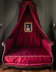 a red canopy bed with a woman's portrait in the corner on top of it