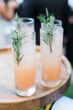 three glasses filled with drinks sitting on top of a wooden table next to each other