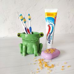 two toothbrushes in a frog shaped container next to a tube of toothpaste