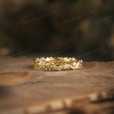 a gold wedding band with green stones on it sitting on top of a piece of wood