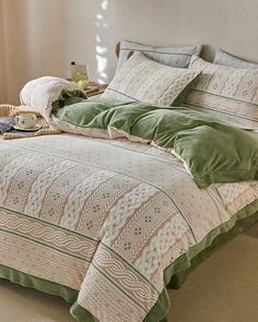 a bed with green comforters and pillows in a room next to a window,