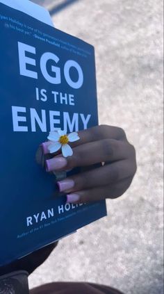 a person holding up a book that says egg is the enemy with a flower on it