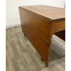 an old wooden desk sitting on top of a hard wood floor next to a white brick wall