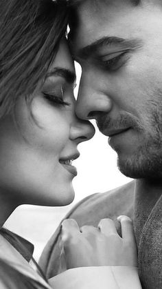 a man and woman are looking at each other while they're kissing in black and white