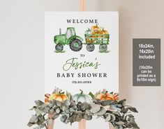 a welcome sign for a baby shower is displayed on a easel with greenery and pumpkins