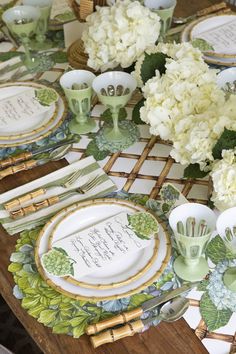 the table is set with green and white plates, silverware, and floral centerpieces