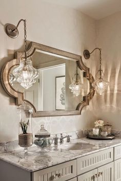 a bathroom with marble counter tops and vanity lights above the sink, along with an ornate mirror