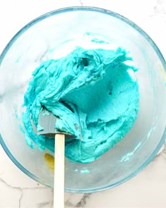 a bowl filled with blue icing and a wooden spoon in it on a marble counter top