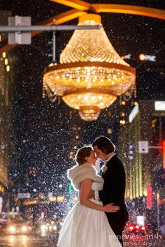 a bride and groom kissing under a chandelier in the rain at their wedding