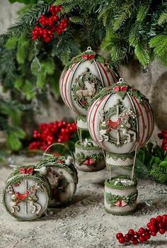 three christmas ornaments sitting on top of a table next to holly wreaths and red berries