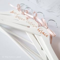 three wooden clothes hangers with name tags on them and pink ribbons attached to them