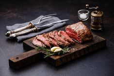 sliced steak on cutting board with knife and salt shaker next to it, along with utensils