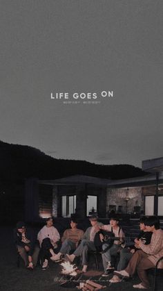 a group of people sitting around a campfire in front of a house with the words life goes on