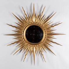 a gold sunburst with black glass in the center on a white wall behind it