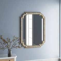 a mirror is hanging on the wall above a dresser and vase with flowers in it