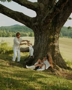 two people sitting on the ground next to a large tree and one person standing up