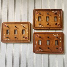 three wooden switch plates sitting on top of a white wall next to each other with flowers painted on them