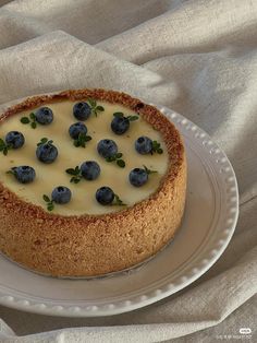 a cheesecake topped with blueberries and green leaves on top of a white plate