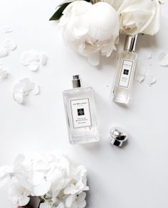 a bottle of cologne next to some flowers on a white surface with petals scattered around it