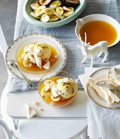 two plates with desserts on them next to bowls of fruit and other food items