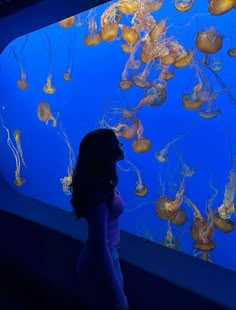 a woman standing in front of a display of jellyfish and other sea creatures at the aquarium