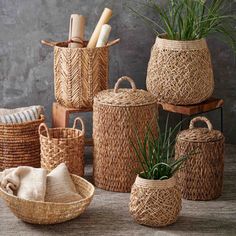 several woven baskets with plants in them sitting on a table next to a gray wall