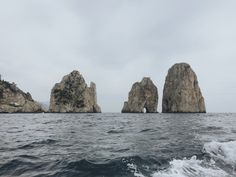 several large rocks sticking out of the water near each other on an overcast day