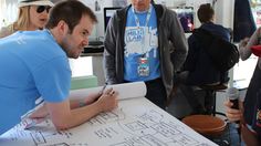 a group of people standing around a white board with blueprint on it and one man holding a pen