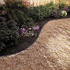 a garden area with gravel and flowers in the foreground, next to a fence